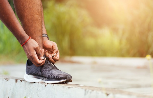 Primo piano corridore sportivo asiatico uomo nero indossare orologio stand passo sul marciapiede provando scarpe da corsa lacci preparandosi per fare jogging e correre all'aperto parco salute strada, concetto di allenamento esercizio sano