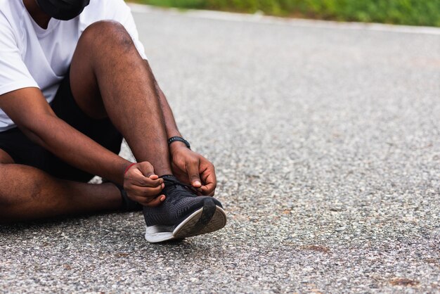Primo piano corridore sportivo asiatico uomo nero seduto laccio delle scarpe provando scarpe da corsa preparandosi per fare jogging e correre sulla strada all'aperto, concetto di allenamento esercizio fisico