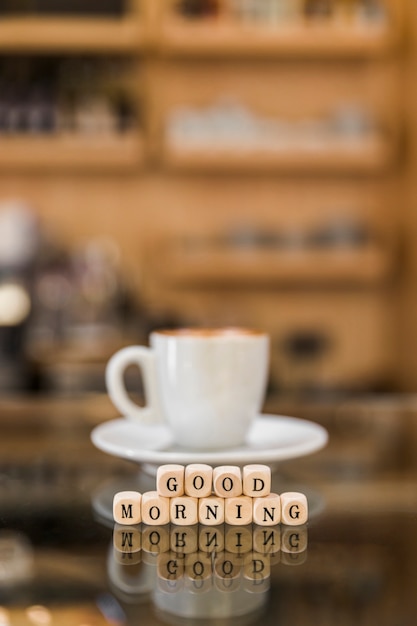 Primo piano dei blocchetti cubici di buongiorno con la tazza di caffè sulla superficie di vetro