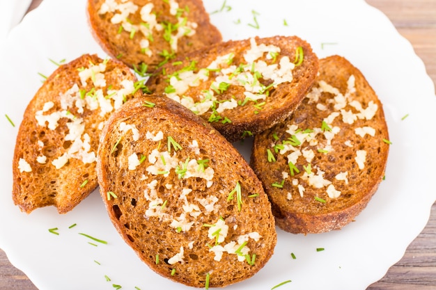 Primo piano dei crostini freschi dell'aglio della segale con aneto su un piatto su una tavola di legno