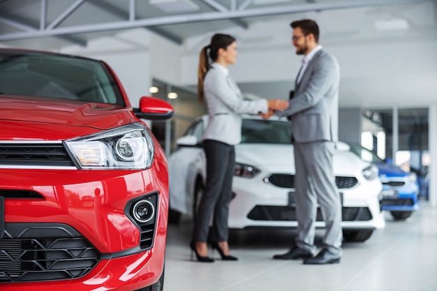 Primo piano dei fari di un'auto. venditore di auto e cliente si stringono la mano.