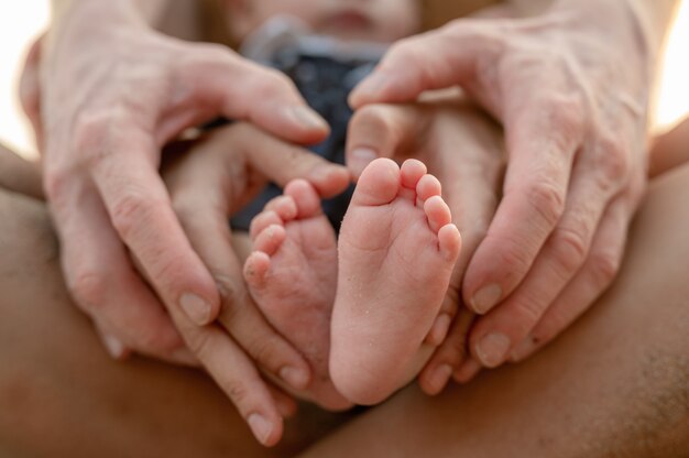 Primo piano dei piedi del bambino. Madre che tiene bambino. Famiglia felice al tramonto. Famiglia in vacanza sulla spiaggia in estate, concetto di viaggio, vacanza e stile di vita