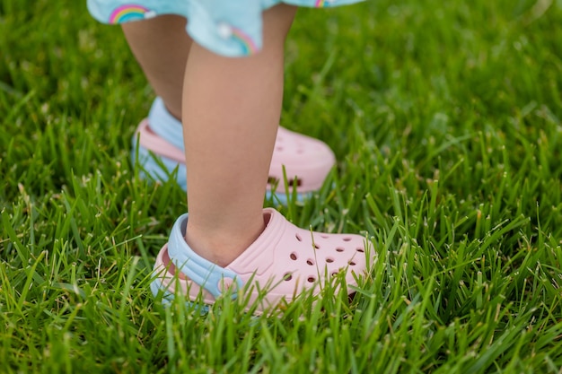 primo piano dei piedi di un bambino, calzato con sandali di gomma rosa, in piedi sull'erba