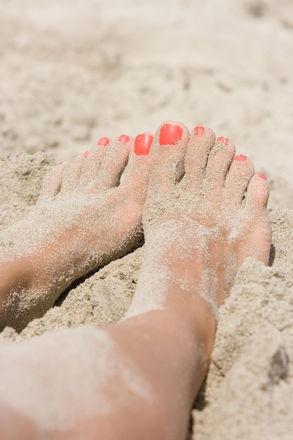 Primo piano dei piedi e delle dita femminili con il pedicure rosso nella sabbia bianca sulla spiaggia