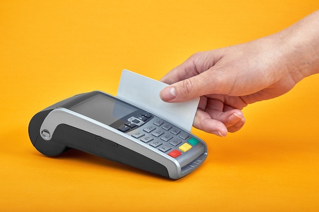 Primo piano dei pulsanti della macchina di pagamento con la mano umana che tiene la carta di plastica vicino sul tavolo giallo