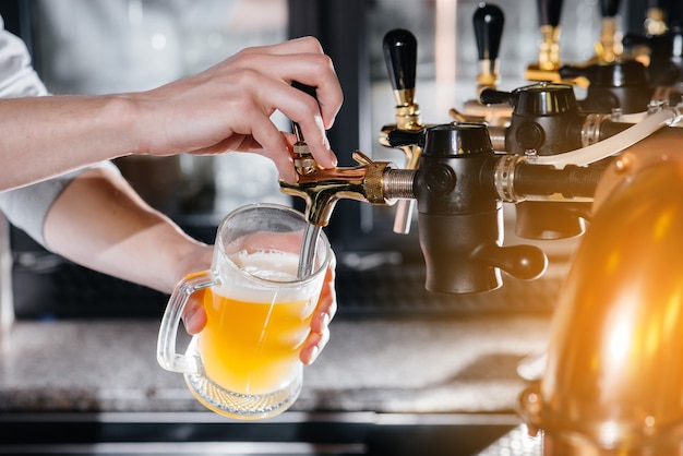 Primo piano del barista che riempie un boccale di birra leggera. Il bancone del bar del pub.