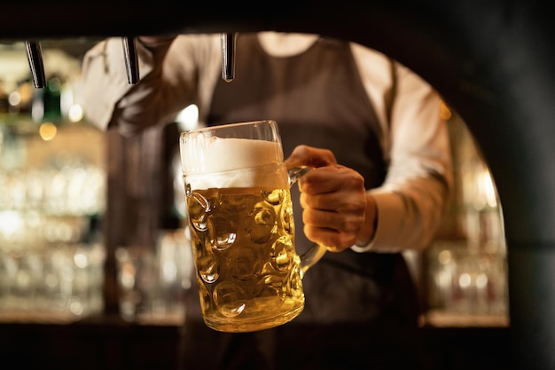 Primo piano del barista che versa birra dal rubinetto della birra mentre lavora in un pub