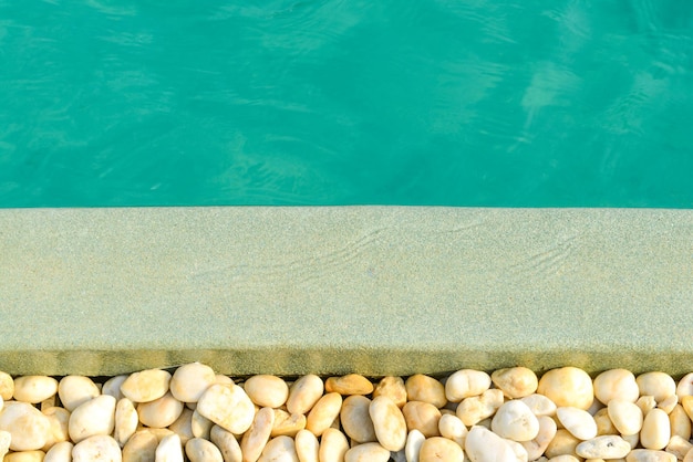 Primo piano del bordo di pietra davanti alla piscina blu brillante. Decorazione e design di piscine con riflesso del sole, vacanza, relax, concetto di fuga