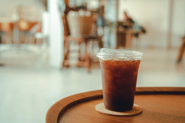 Primo piano del caffè ghiacciato americano o caffè nero in tazza tazza sulla scrivania in legno scrivania da ufficio nella caffetteria al bar in giardino durante il concetto di lavoro aziendale