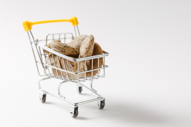 Primo piano del carrello della spesa del supermercato per lo shopping con elementi in plastica gialla sul manico riempito con pietre marroni isolate su sfondo bianco. Concetto di acquisto. Copia spazio per la pubblicità.