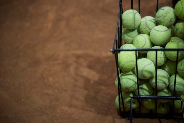 Primo piano del cestino nero con palline da tennis sul campo Cestino nero con palline da tennis