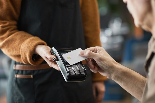 Primo piano del cliente del bar che mette la carta di credito con NFC sul terminale tenuto dalla cameriera mentre paga il pranzo