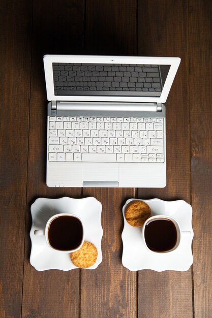 Primo piano del computer portatile con due tazze di caffè nero con i biscotti sulla tavola di legno