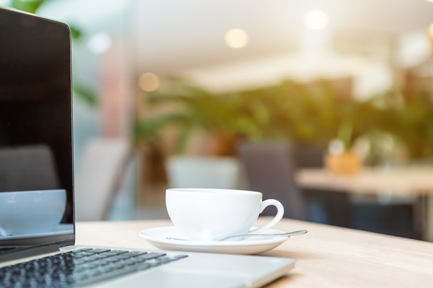 Primo piano del computer portatile di affari e della tazza di caffè sulla tavola di legno nella caffetteria