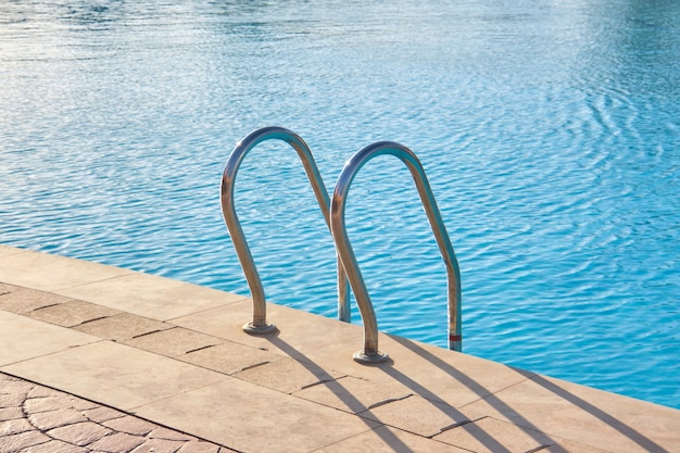 Primo piano del corrimano in acciaio inossidabile della piscina che scende nell'acqua chiara della piscina tartaruga. Accessibilità del concetto di attività ricreative.