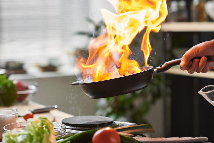 Foto primo piano del cuoco unico che tiene la padella che frigge la carne sul fuoco aperto