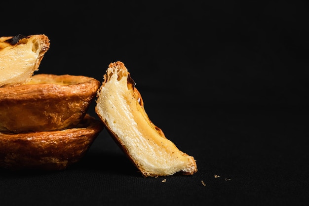 Primo piano del dessert Pastel de nata, tagliato a metà che mostra il ripieno di crema pasticcera, su sfondo nero, scuro e lunatico