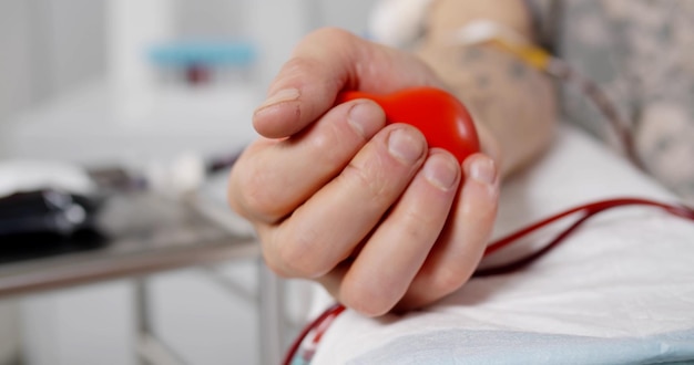 Primo piano del donatore di sangue che schiaccia il bulbo di gomma a forma di cuore in mano