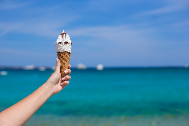 Primo piano del gelato saporito nel fondo femminile della mano il mare del turchese