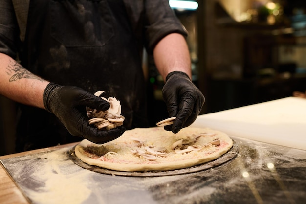 Primo piano del giovane chef che mette i funghi tritati freschi sulla focaccia