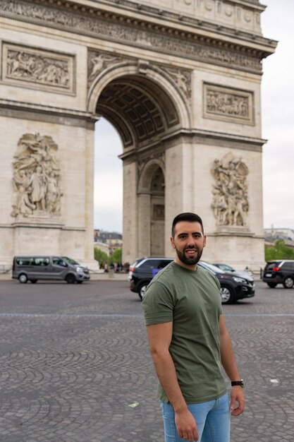 Primo piano del giovane con la barba sorridente e felice e dietro di lui l'Arco di Trionfo a Parigi