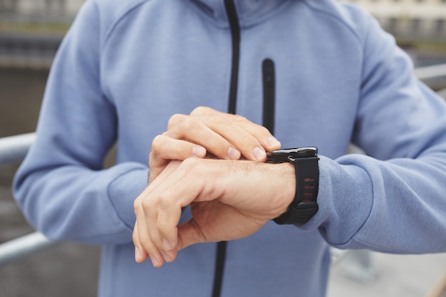 Primo piano del giovane controllando il suo polso sul braccialetto fitness durante il suo jogging all'aperto