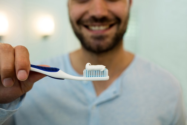 Primo piano del giovane felice che tiene lo spazzolino da denti con dentifricio in pasta a casa