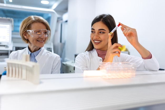 Primo piano del giovane medico in biochimica che analizza e tiene in mano la provetta con un campione di materiale genetico Ricercatore di chimica in laboratorio sterile utilizzando la tecnologia moderna per testare il liquido microbiologico