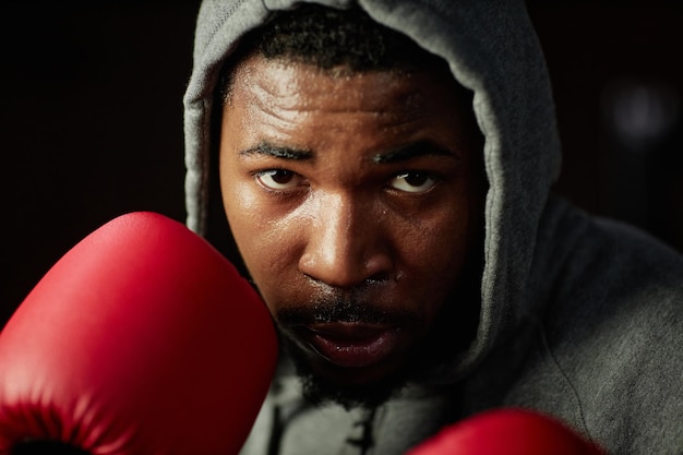 Primo piano del giovane pugile maschio afroamericano che si concentra sul calcio successivo mentre si trova davanti al sacco da boxe e lo colpisce