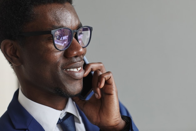 Primo piano del giovane uomo d'affari africano in occhiali sorridente mentre parla sul telefono cellulare