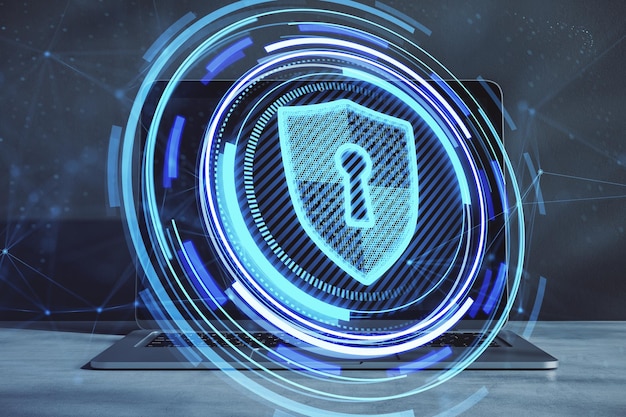 Primo piano del laptop sul desktop con ologramma creativo a scudo blu brillante su sfondo sfocato Database di sicurezza sicuro e concetto di protezione web Doppia esposizione