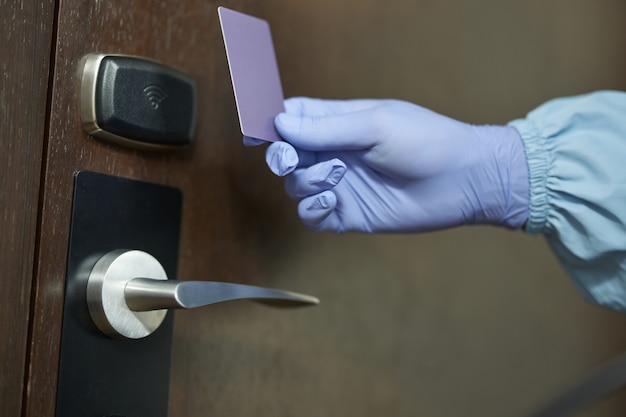 Primo piano del lavoratore in tuta blu e guanti protettivi che tengono la carta davanti alla porta della stanza. Coronavirus e concetto di quarantena