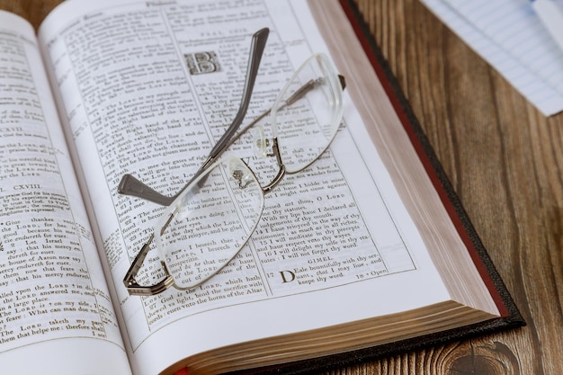 Primo piano del martelletto del giudice sul libro del mondo biblico su un tavolo di legno con gli occhiali per leggere un libro