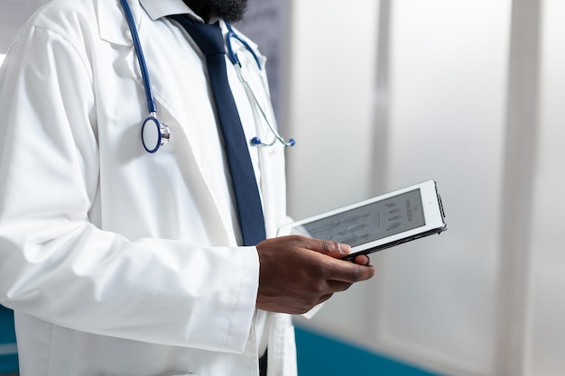 Primo piano del medico afroamericano che tiene in mano un computer tablet che analizza la prescrizione della medicina durante l'appuntamento medico. Terapeuta che lavora al trattamento sanitario nell'ufficio dell'ospedale