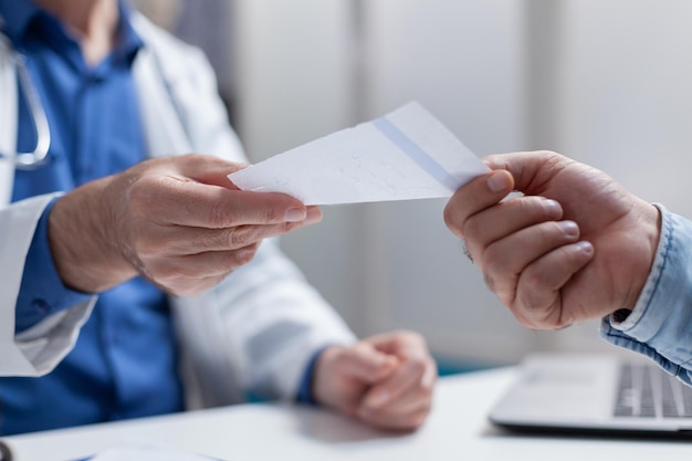 Primo piano del medico che dà la carta di prescrizione al paziente all'appuntamento di controllo. Medico che distribuisce documento per il trattamento e la medicina contro la malattia. Persone che si incontrano alla consultazione