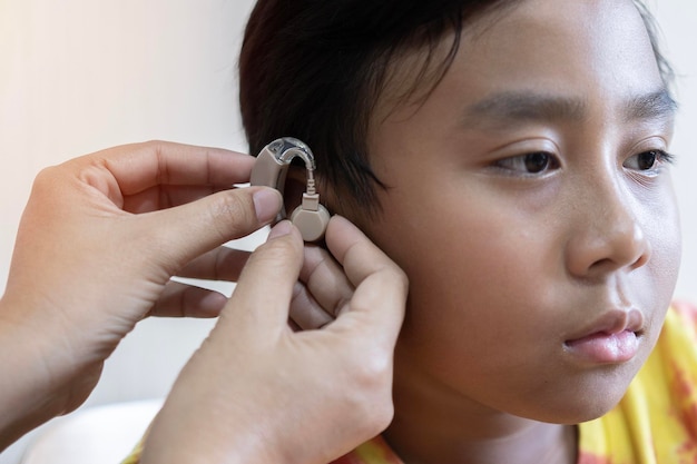 Primo piano del medico che inserisce l'apparecchio acustico nell'orecchio di un ragazzo asiatico Perdita dell'udito nel concetto di infanzia