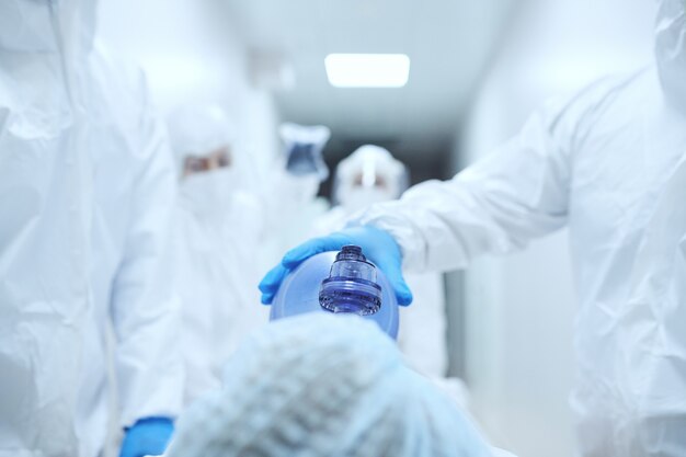 Primo piano del medico in uniforme protettiva che mette la maschera di ossigeno sul viso del paziente prima dell'operazione