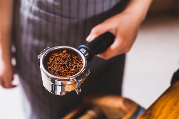 Primo piano del mestolo del caffè espresso della tenuta della mano di barista femminile con polvere di caffè