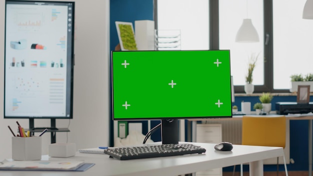 Primo piano del monitor con schermo verde alla scrivania vuota. Nessuno nell'ufficio di avvio con chiave di crominanza e modello di simulazione isolato sul display del computer. Spazio copia mock-up con schermo vuoto.
