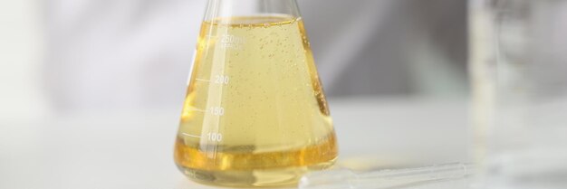 Primo piano del pallone con liquido giallo sul tavolo del concetto di laboratorio di ricerca di prodotti chimici e