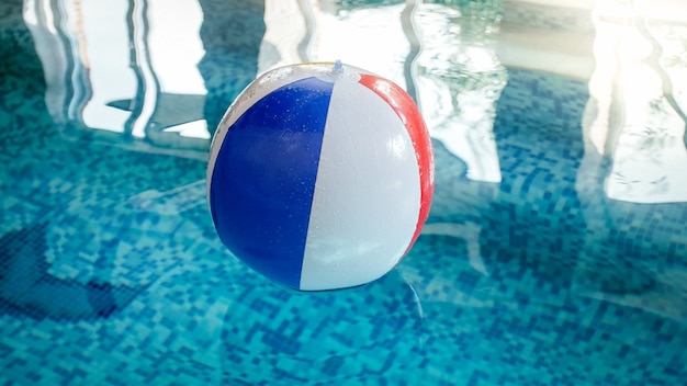 Primo piano del pallone da spiaggia gonfiabile a strisce colorate che galleggia sulla superficie dell'acqua in piscina