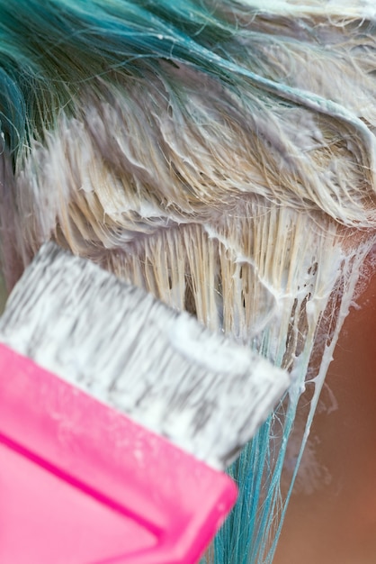 Primo piano del parrucchiere con pennello rosa durante l'applicazione di vernice al cliente femminile con capelli color smeraldo co...