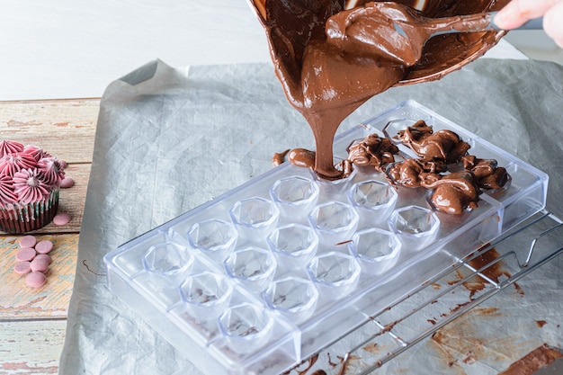 Primo piano del pasticcere che versa il cioccolato temperato in una forma del policarbonato.