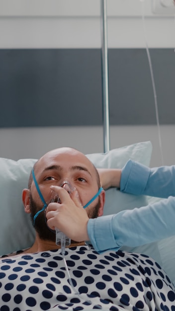 Primo piano del paziente malato che riposa a letto mentre il medico mette la maschera di ossigeno per monitorare la malattia respiratoria nel reparto ospedaliero durante l'emergenza sanitaria. Medico che analizza il battito cardiaco più