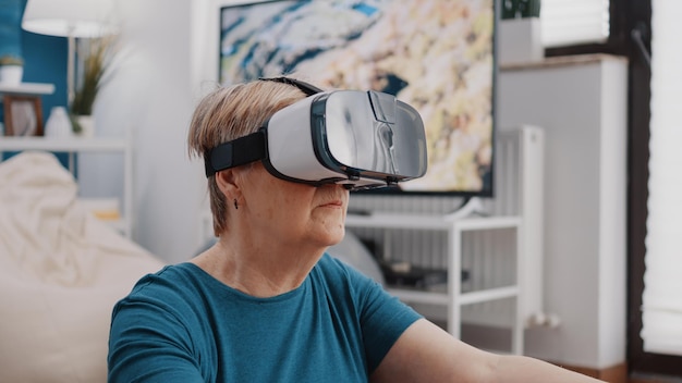 Primo piano del pensionato che medita con gli occhiali vr a casa. Donna in pensione che fa yoga e meditazione, utilizzando occhiali con tecnologia di realtà virtuale prima dell'allenamento e dell'esercizio fitness.