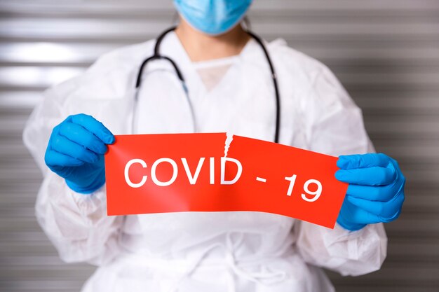 Primo piano del personale sanitario che indossa maschere chirurgiche e guanti protettivi in possesso di un cartone con testo Covid19