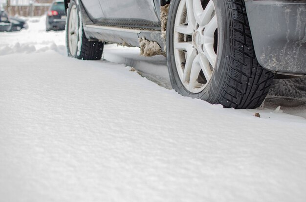 Primo piano del pneumatico dell'auto sulla strada invernale ricoperta di neve. I fiocchi di neve sono sulla ruota di gomma.