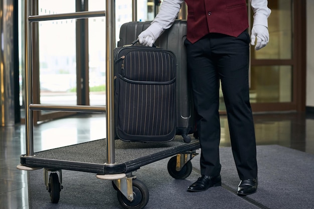 Primo piano del portiere in uniforme che mette i bagagli sul carrello nella hall dell'hotel