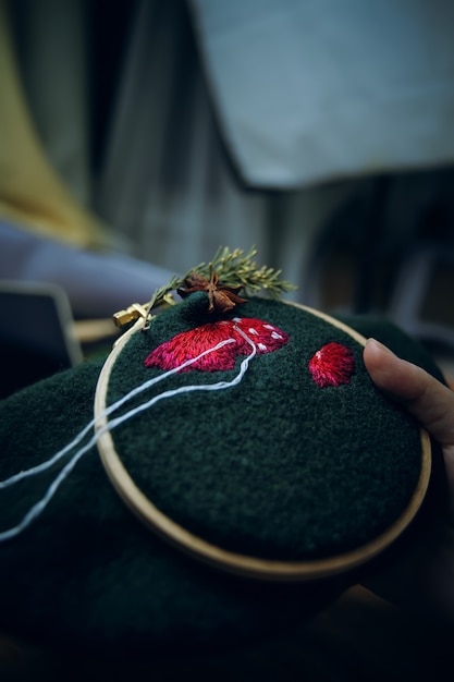 Primo piano del ricamo del cappello a fungo in un cerchio di legno su mani di donna materiale verde che fanno con...