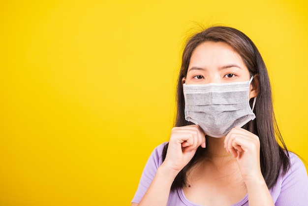 Primo piano del ritratto asiatico giovane donna adolescente che indossa una maschera protettiva contro il coronavirus o il virus COVID-19 che mostra la dimostrazione del passo corretto, studio girato isolato sfondo giallo